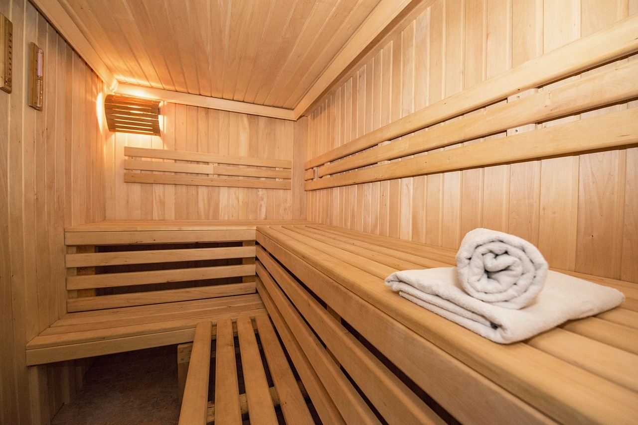 Warm-lit indoor sauna interior with tiered cedar benches and rolled towels.
